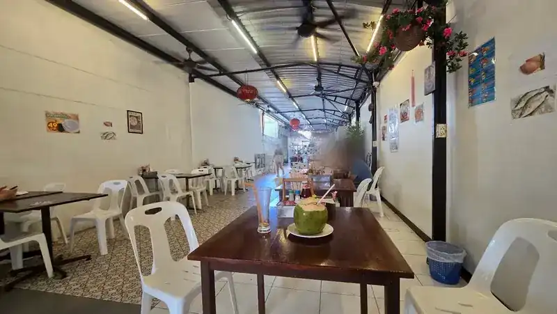 The long dining hall with wooden tables, white chairs, ceiling fans and red lanterns, a fresh coconut on the table in front