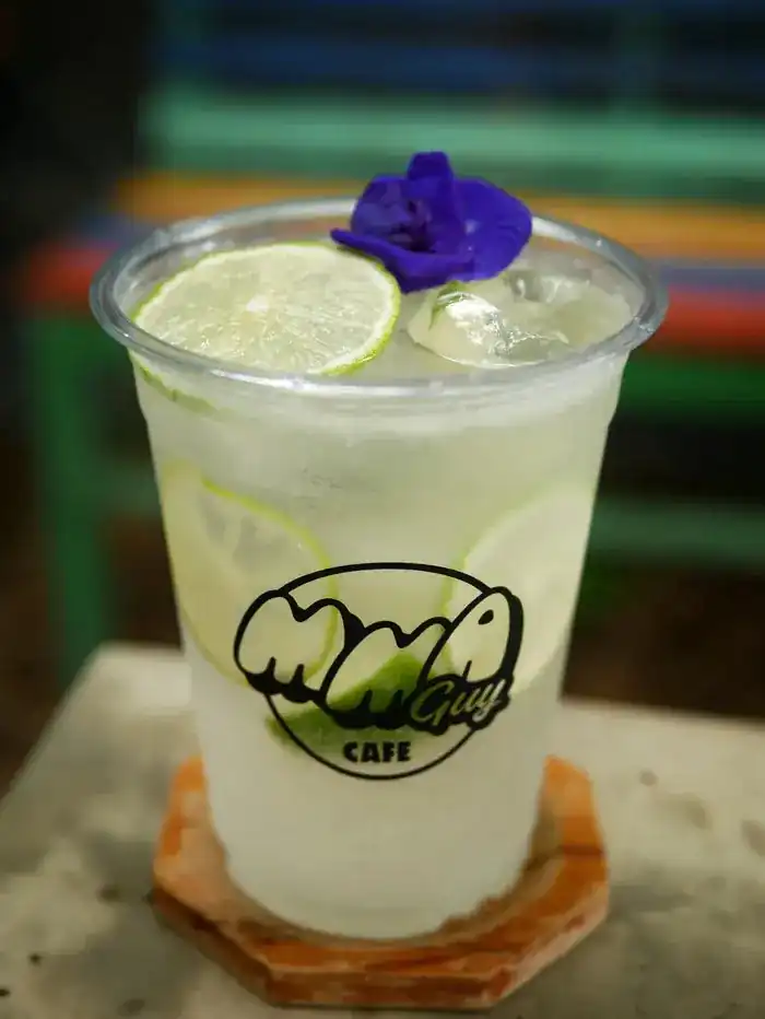Fresh limeade with lime slices and a butterfly pea flower, in an MMA GUY Cafe cup