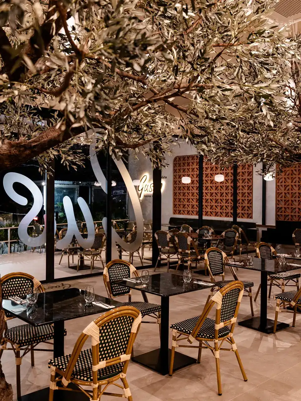 Rattan chairs and marble tables under the olive tree in Gusto's dining room