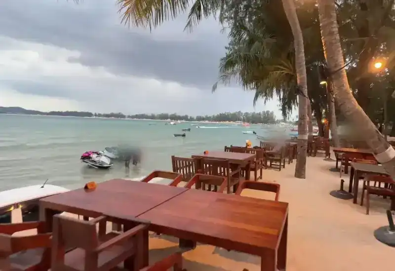 Wooden tables on the beach facing the sea, with lights in the palms along the sand