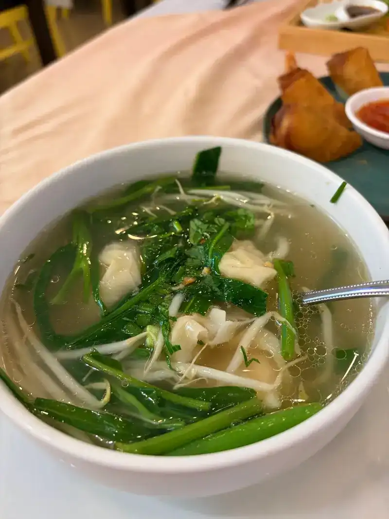 A bowl of clear wonton soup with morning glory and bean sprouts