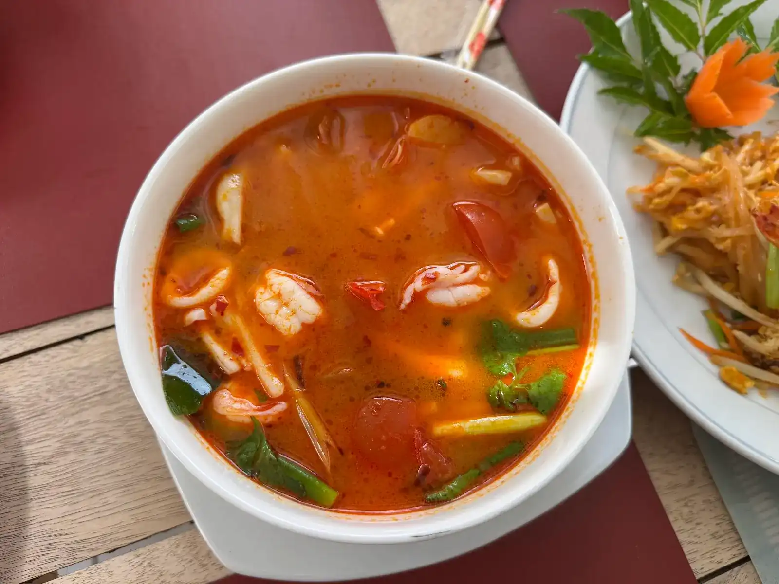 Tom yum with prawns and squid in a white bowl, pad thai beside it