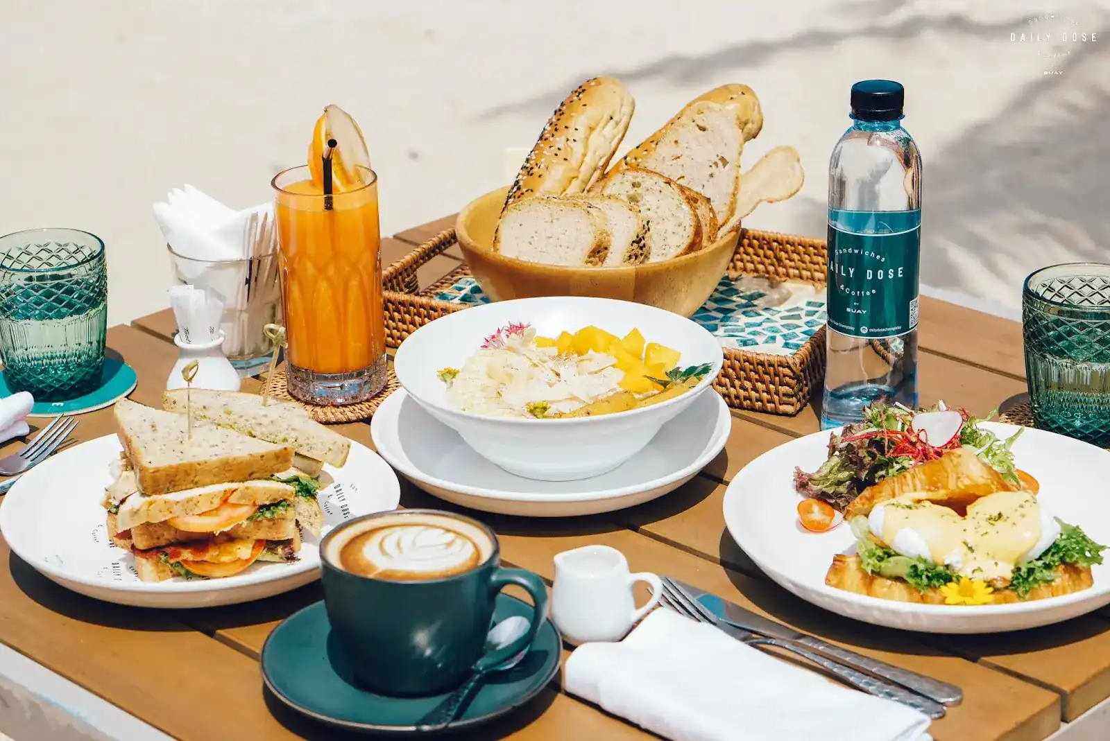 A breakfast table: sandwich, croissant with hollandaise and salad, a bowl topped with mango, bread basket, latte and juice / โต๊ะอาหารเช้า: แซนด์วิช ครัวซองต์ราดซอสฮอลันเดซกับสลัด ชามท็อปมะม่วง ตะกร้าขนมปัง ลาเต้ และน้ำผลไม้