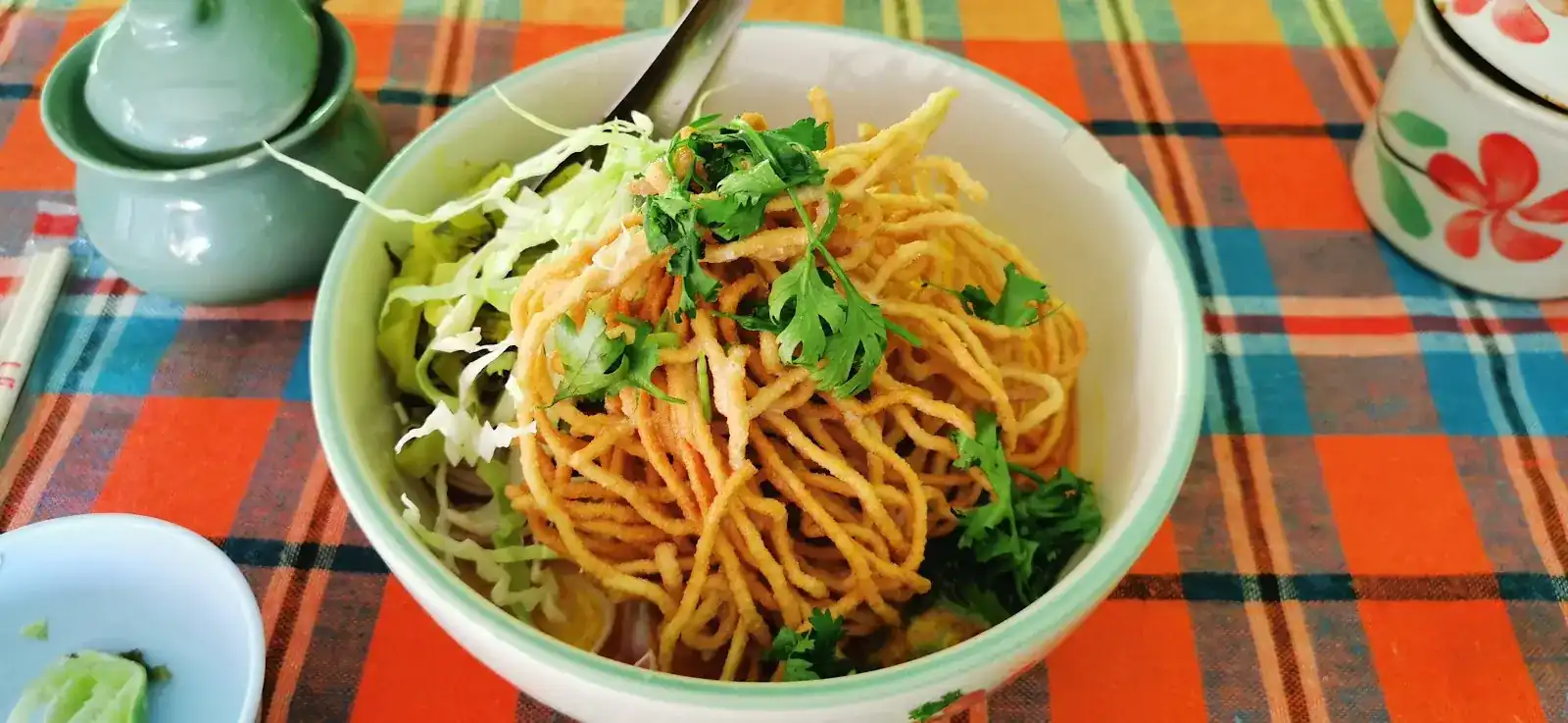 Khao soi topped with crispy noodles, on an orange and blue checked tablecloth