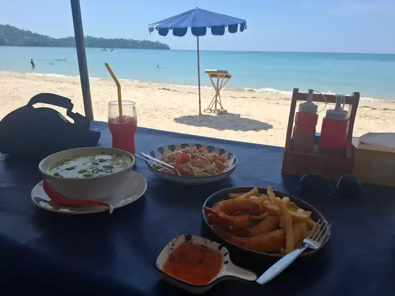 A green curry, papaya salad and fried prawns with chips on a table facing the beach