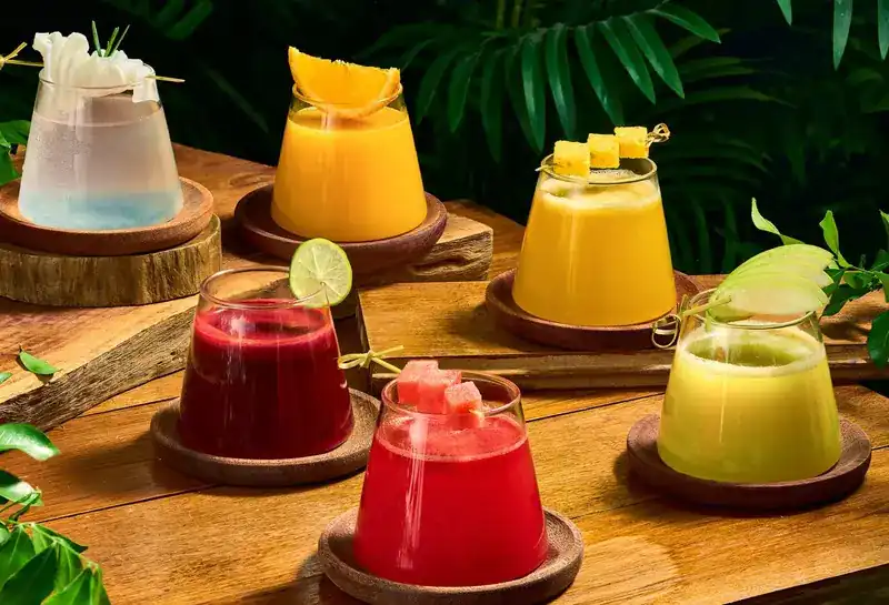 Six fresh juices and coolers in red, orange and yellow on wooden coasters