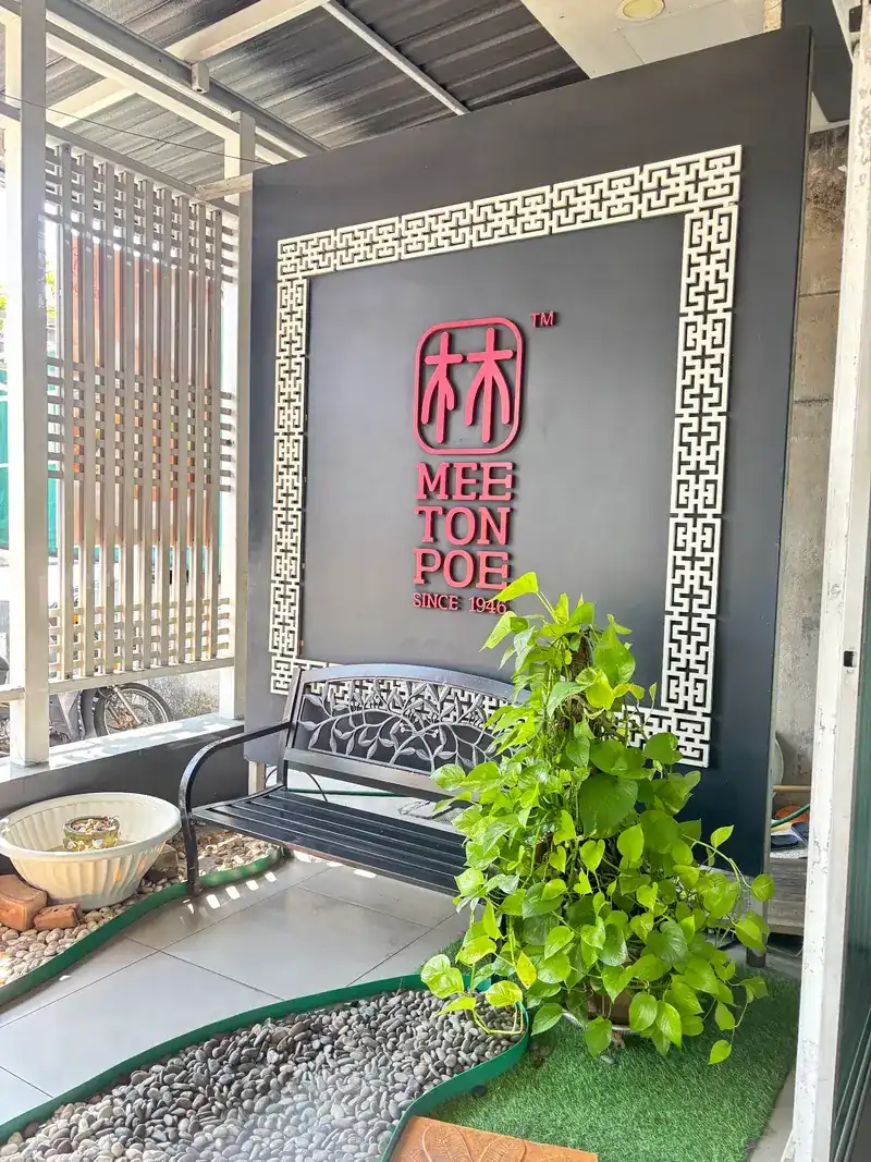 The entrance: the red Mee Ton Poe mark on a dark wall framed in white Chinese lattice, with a bench and a potted plant