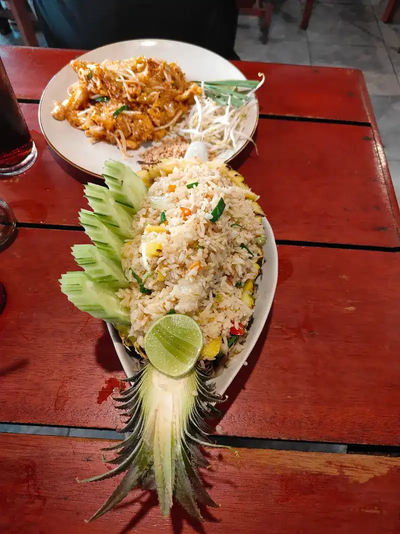 Pineapple fried rice served in half a pineapple, with pad thai behind