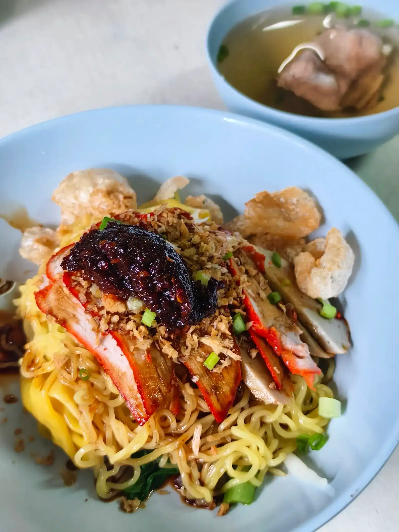 Egg noodles with red pork and crispy toppings, a cup of soup on the side
