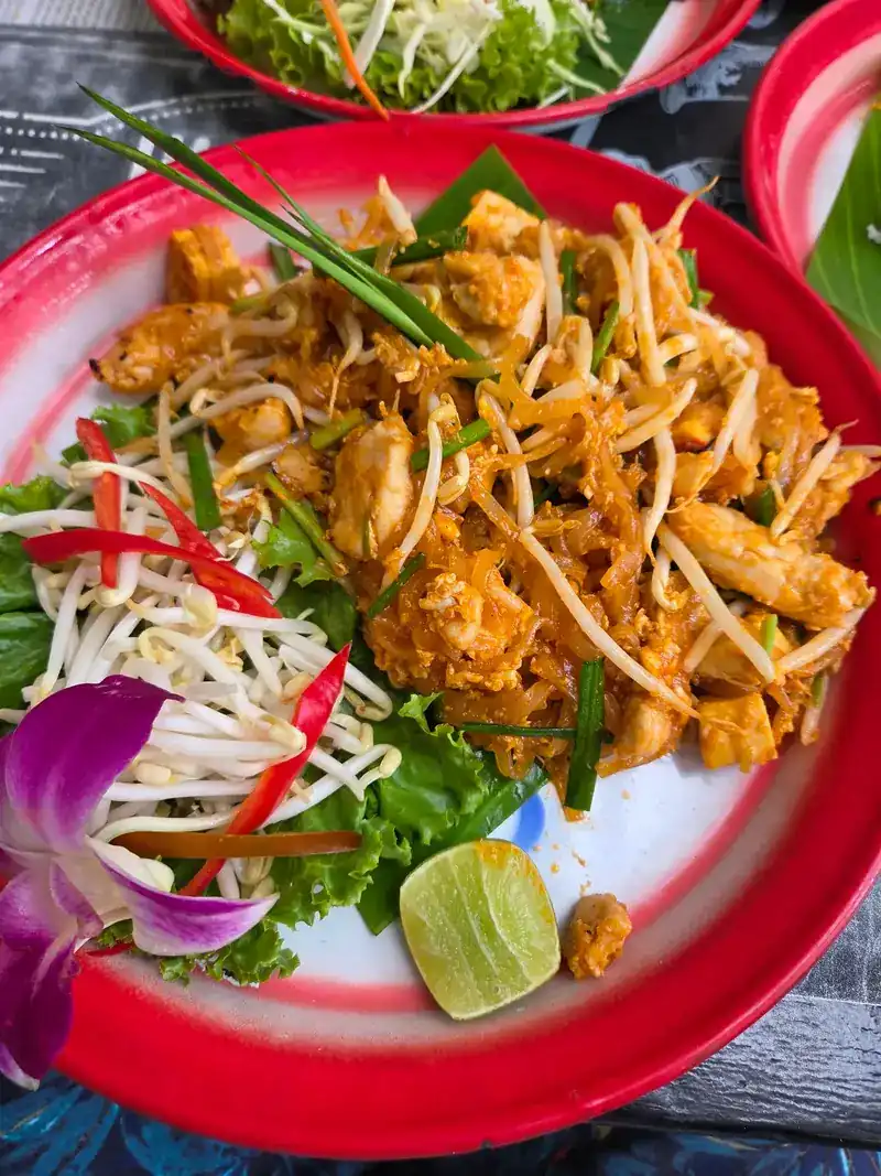 Pad thai with bean sprouts, lime and an orchid on a red-rimmed enamel plate