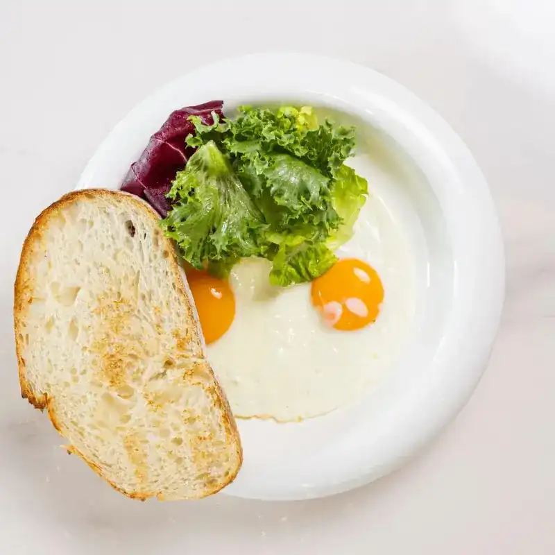 Fried eggs with salad leaves and toasted bread on a white plate
