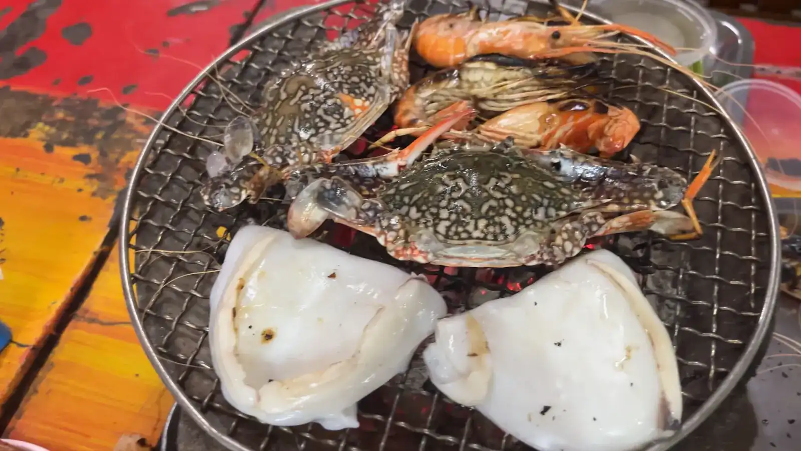 Two crabs, shrimp and squid grilling on the round charcoal grill