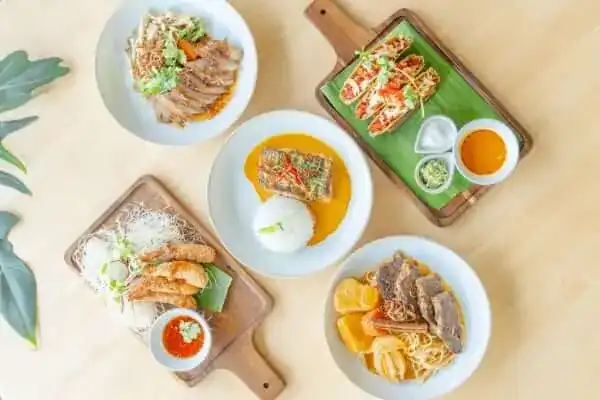 Five dishes seen from above on plates and wooden boards, on a pale table