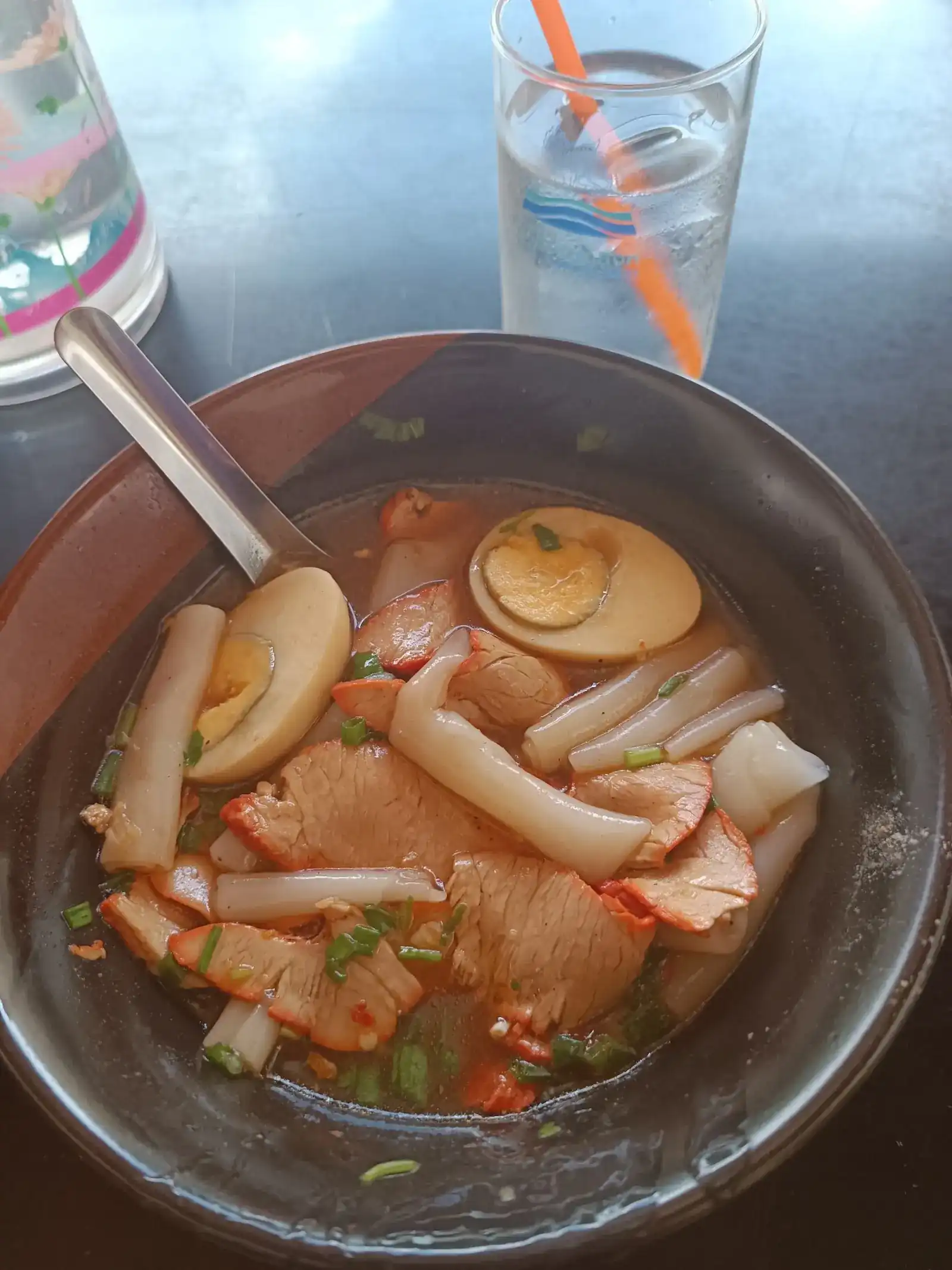 A bowl of kuay jap: rolled rice noodles, red pork, halved eggs and spring onion in broth