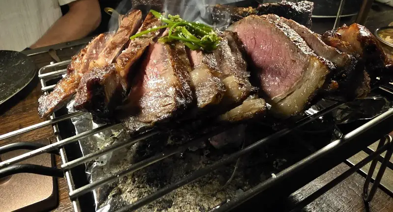 Sliced bone-in steak on a grill rack over embers / สเต๊กเนื้อติดกระดูกหั่นชิ้นบนตะแกรงเหนือถ่าน