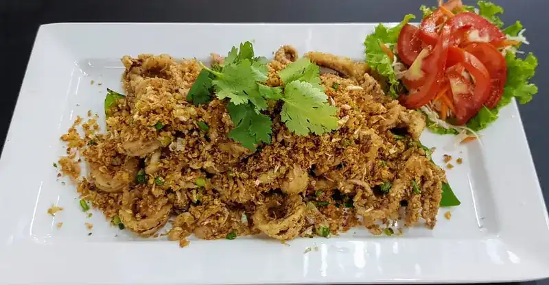 Garlic squid on a white plate with coriander and sliced tomato