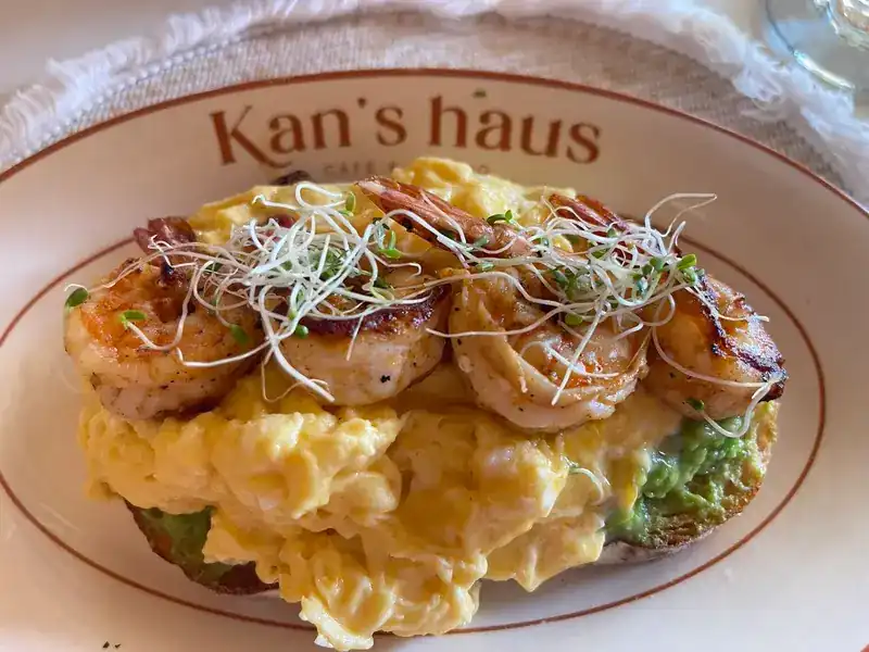 Grilled shrimp on scrambled egg and smashed avocado on toast, on a Kan's haus plate