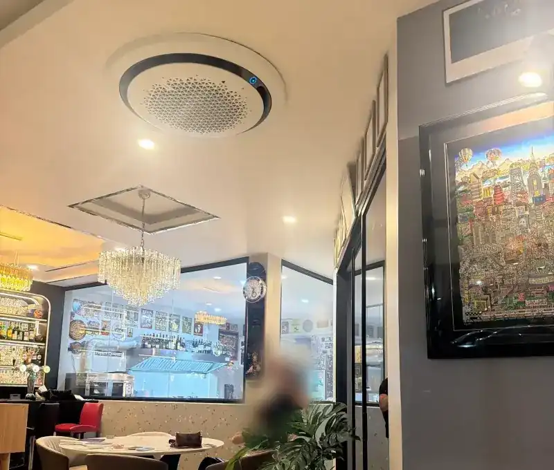 Dining room with a crystal chandelier, round white tables and a large, colourful framed painting