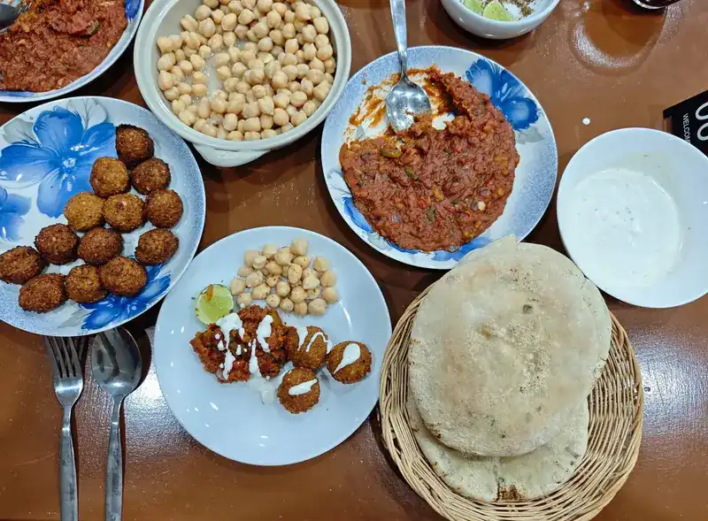 A breakfast spread from above: falafel, chickpeas, dips and a basket of fresh bread