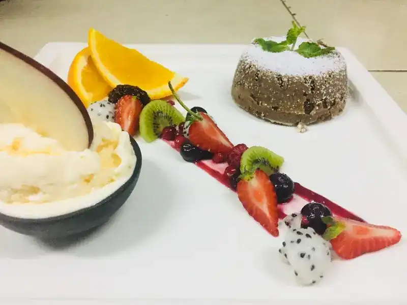 A dessert plate: a small cake dusted with sugar, ice cream in a coconut shell and fresh fruit