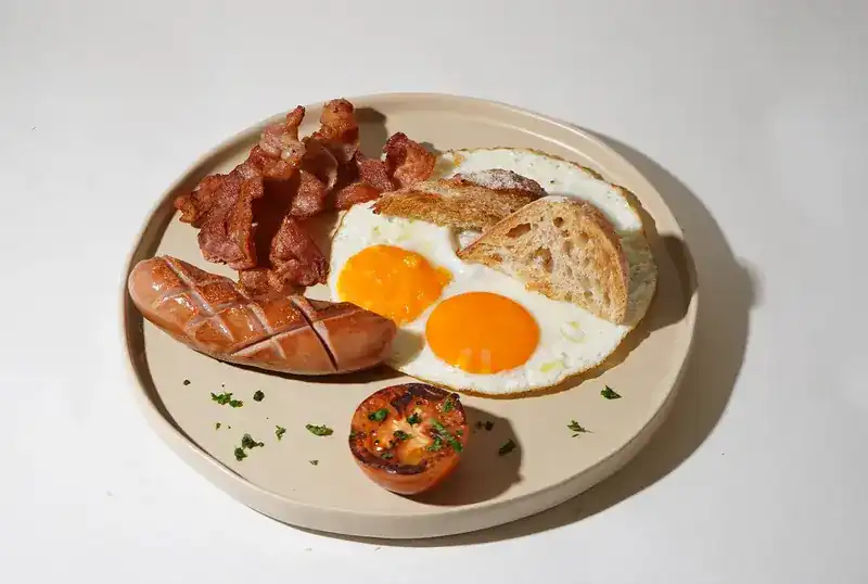 Breakfast plate with two fried eggs, bacon, sausage, toast and a grilled tomato