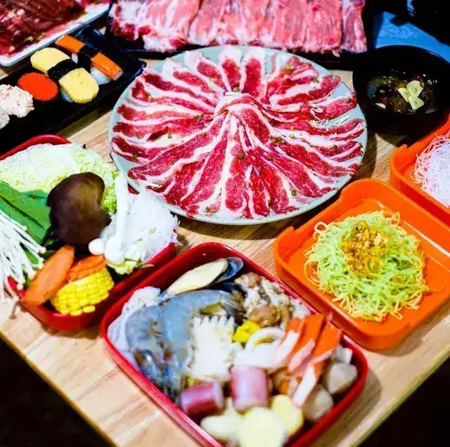 A shabu table set with sliced beef, vegetables, noodles and a seafood tray