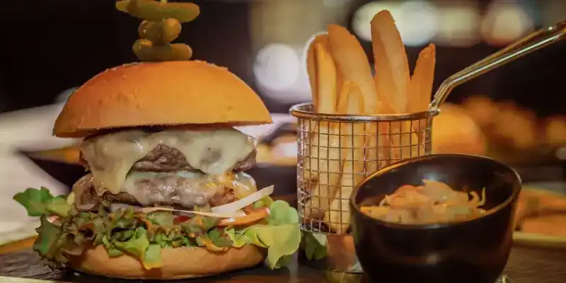 A cheeseburger with lettuce beside a wire basket of fries