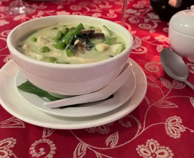 A bowl of green curry on the red tablecloth