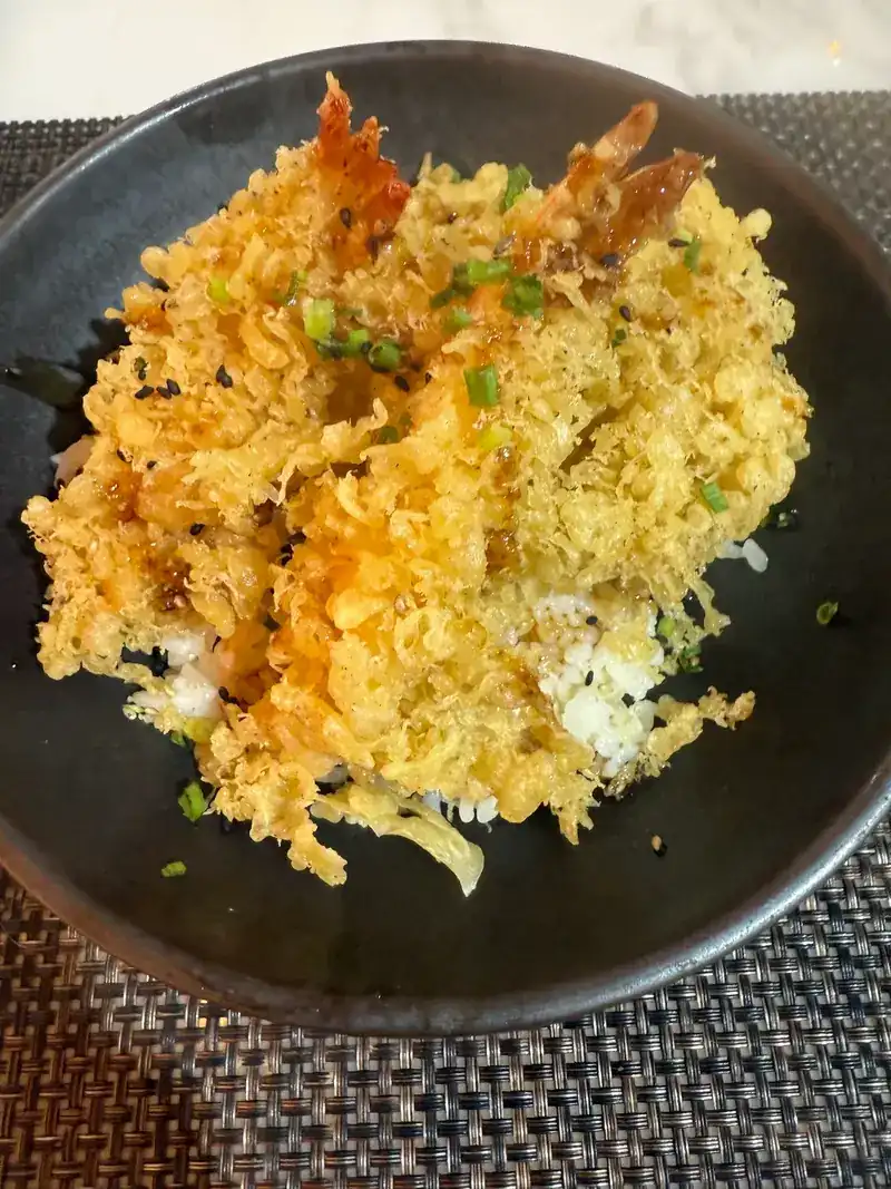 Shrimp tempura over rice in a black bowl