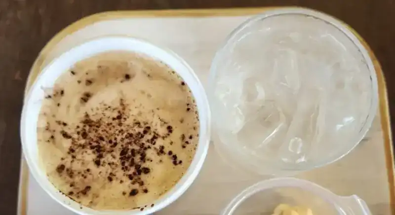 A cup of hot coffee with a glass of ice on a tray