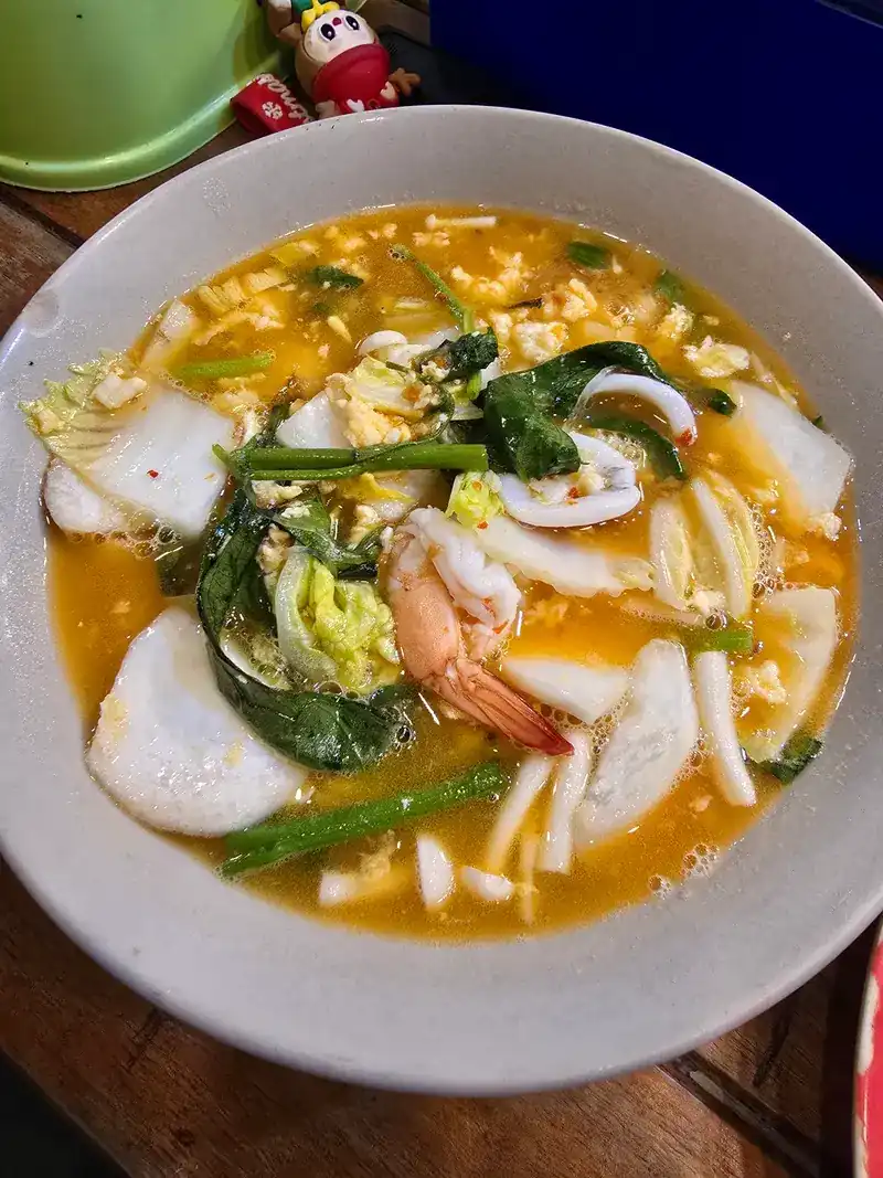 A bowl of soup with squid, shrimp, egg, cabbage and morning glory