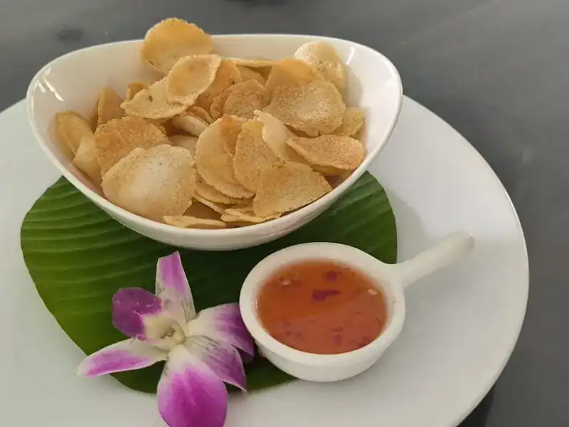 Crackers in a white bowl with a sweet chilli dip and a pink orchid