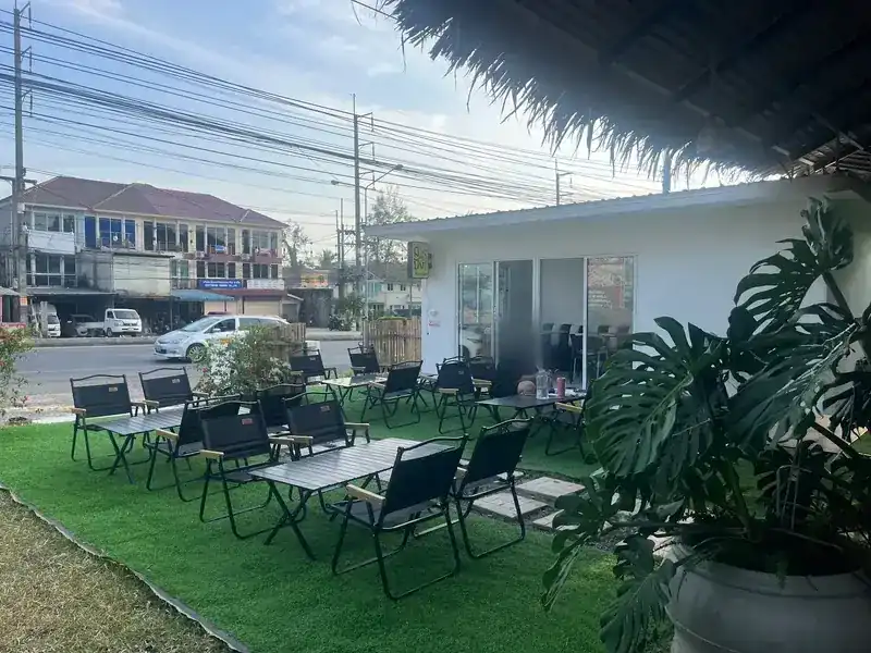 Black folding tables and chairs on a green lawn beside a small white shop by the road