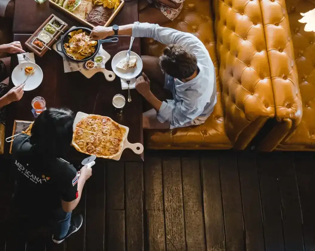 A table between mustard leather booths, seen from above: nachos, a pizza on a board and shared plates