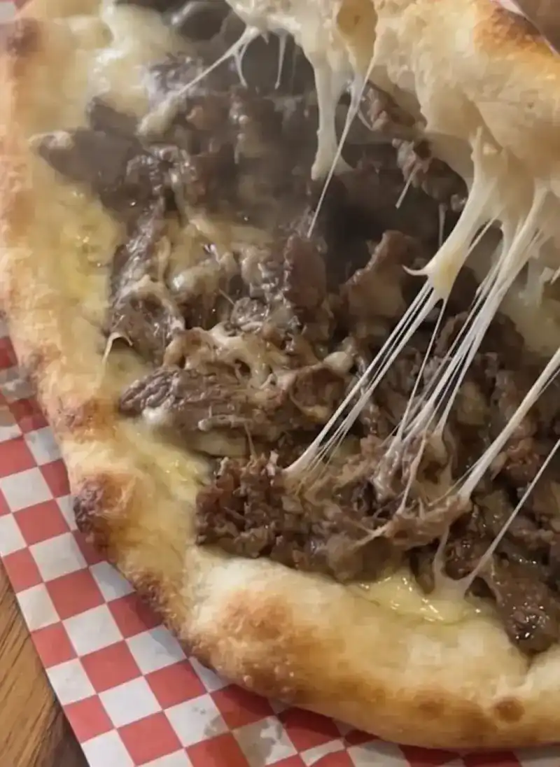 A baked flatbread with a meat filling, melted cheese stretching as it is pulled apart