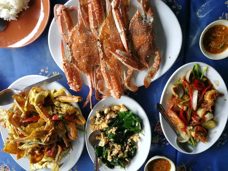 A table seen from above: whole blue crabs, greens stir-fried with egg, prawns with chilli and onion, and a fried dish with dipping sauces