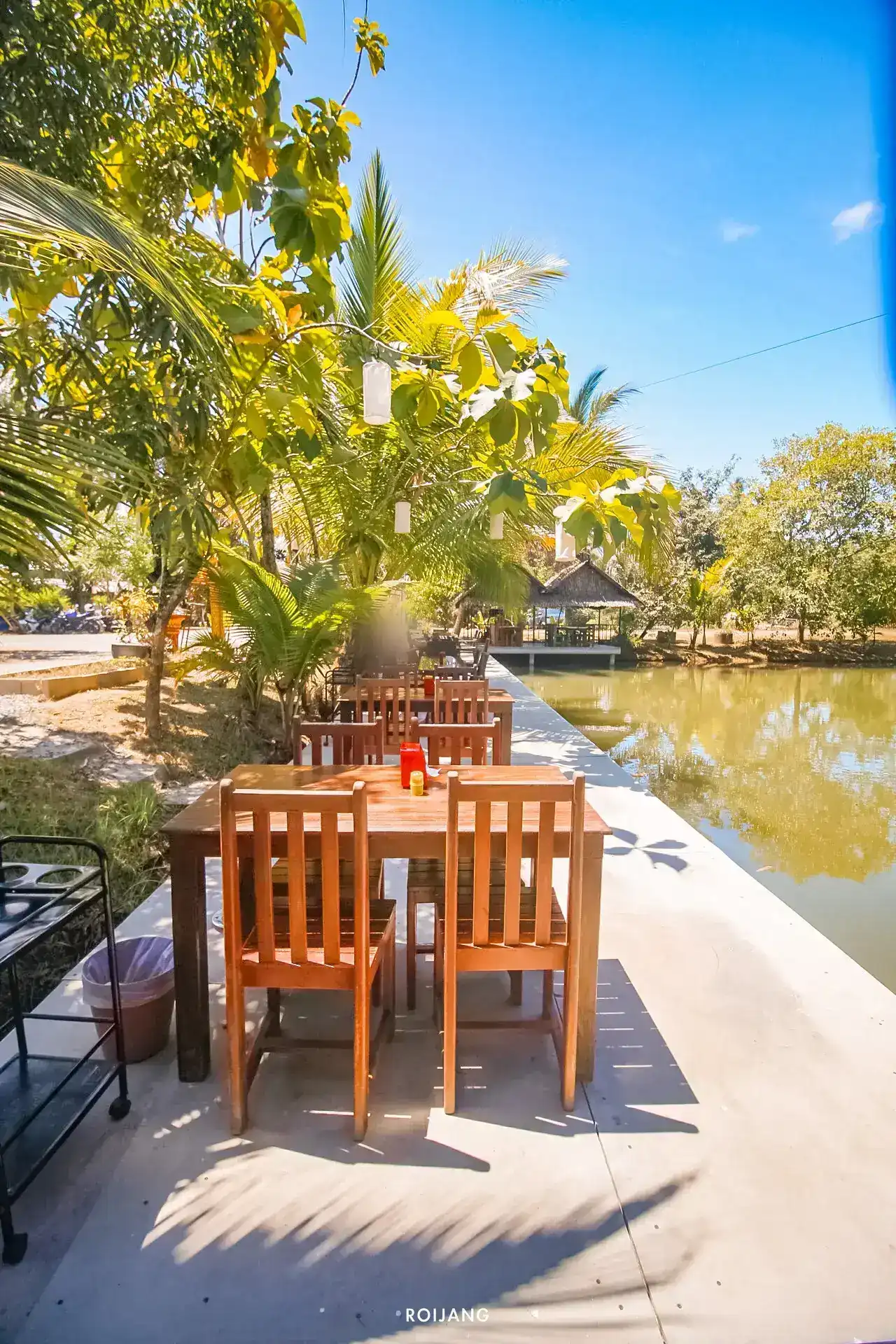 Wooden tables along the edge of the pond, under palm trees