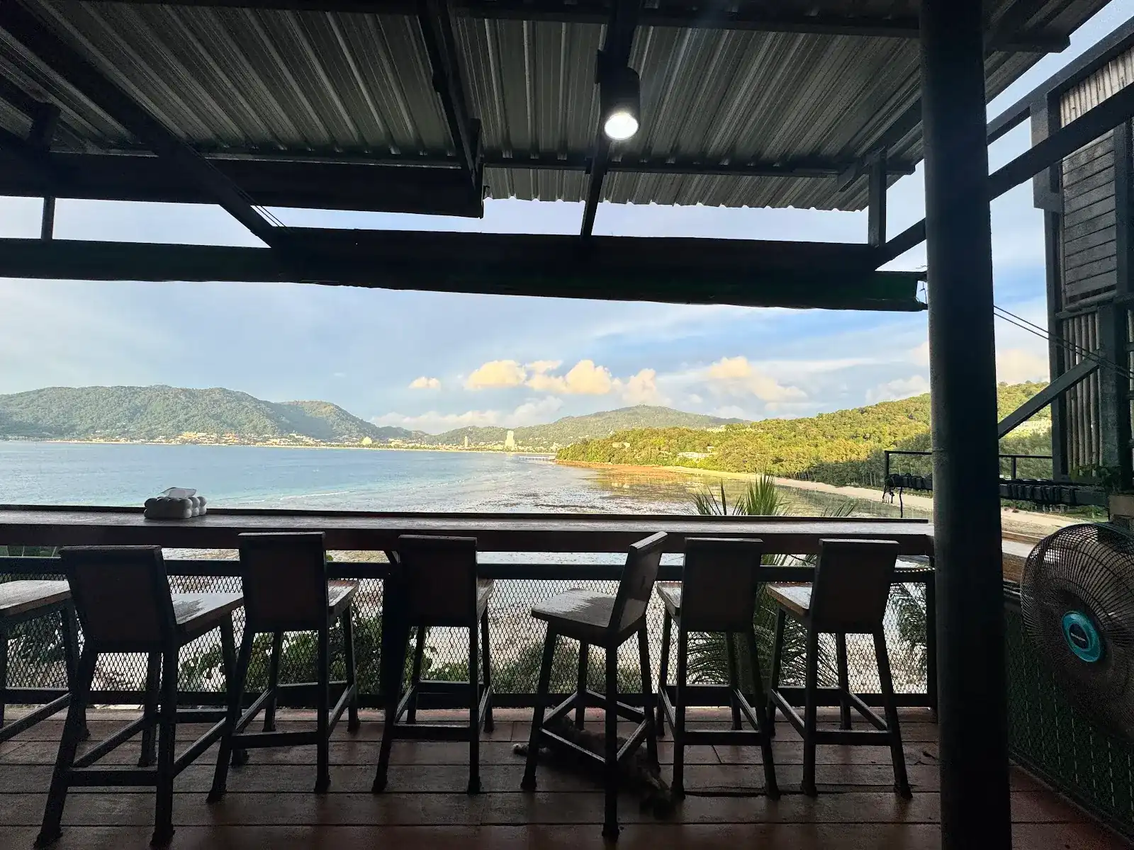 High stools along the terrace railing, looking out over Patong Bay and the hills in late afternoon light