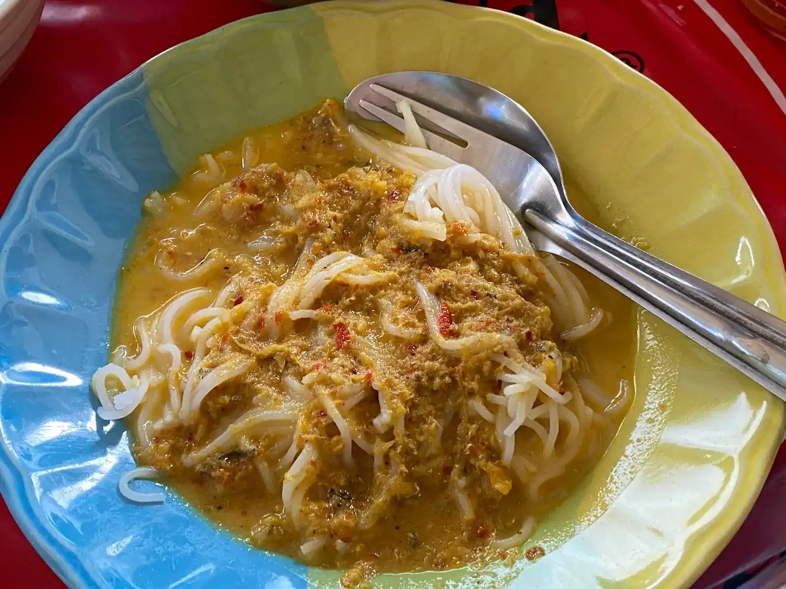 Khanom jeen rice noodles under a yellow curry, in a blue and yellow plate