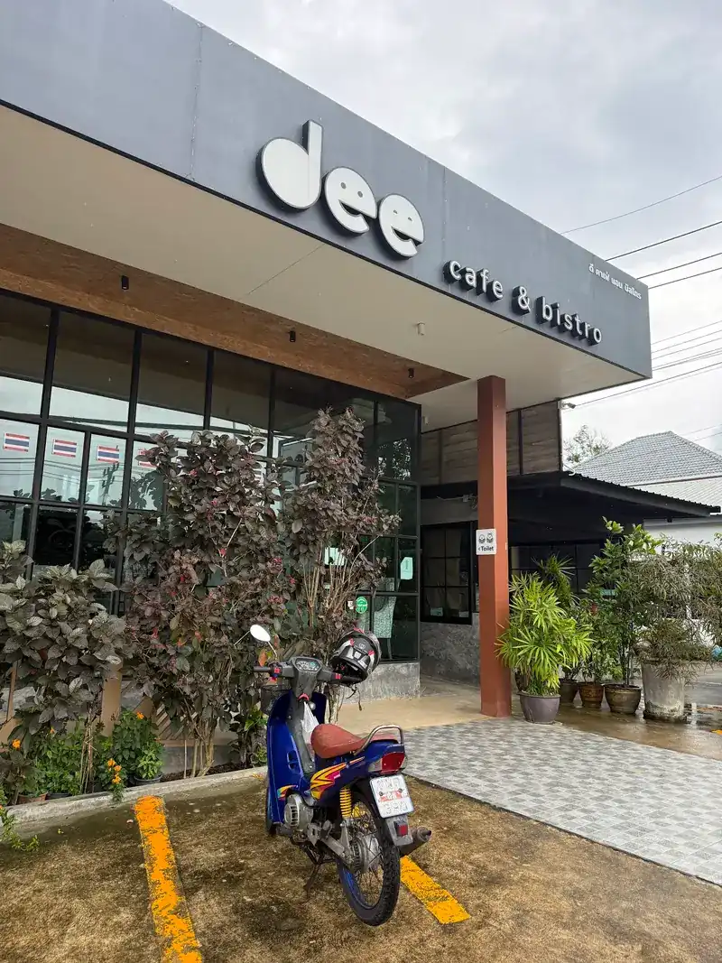 The front of dee cafe & bistro with its sign, plants and parking