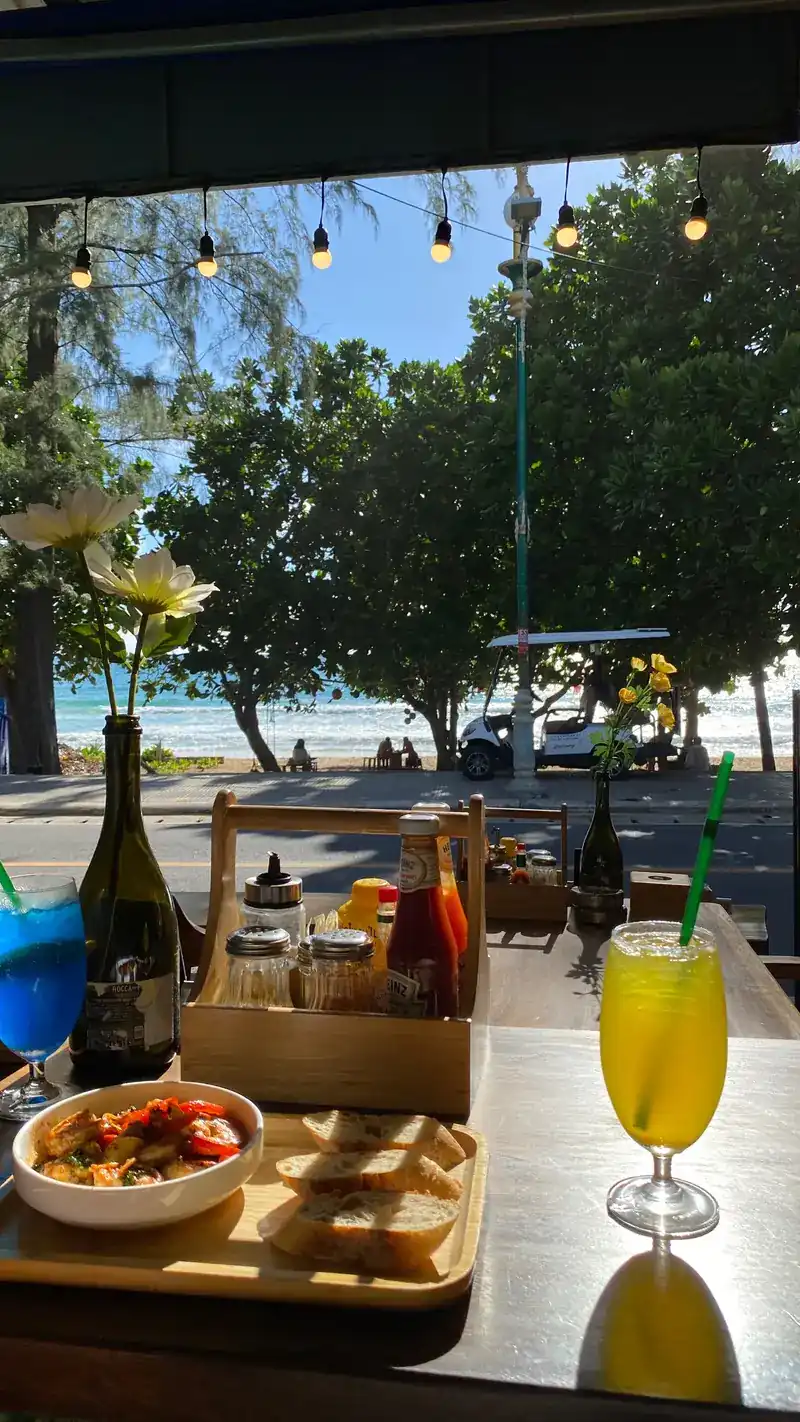 A table at the open front with drinks and a small plate, looking out to the trees and the beach