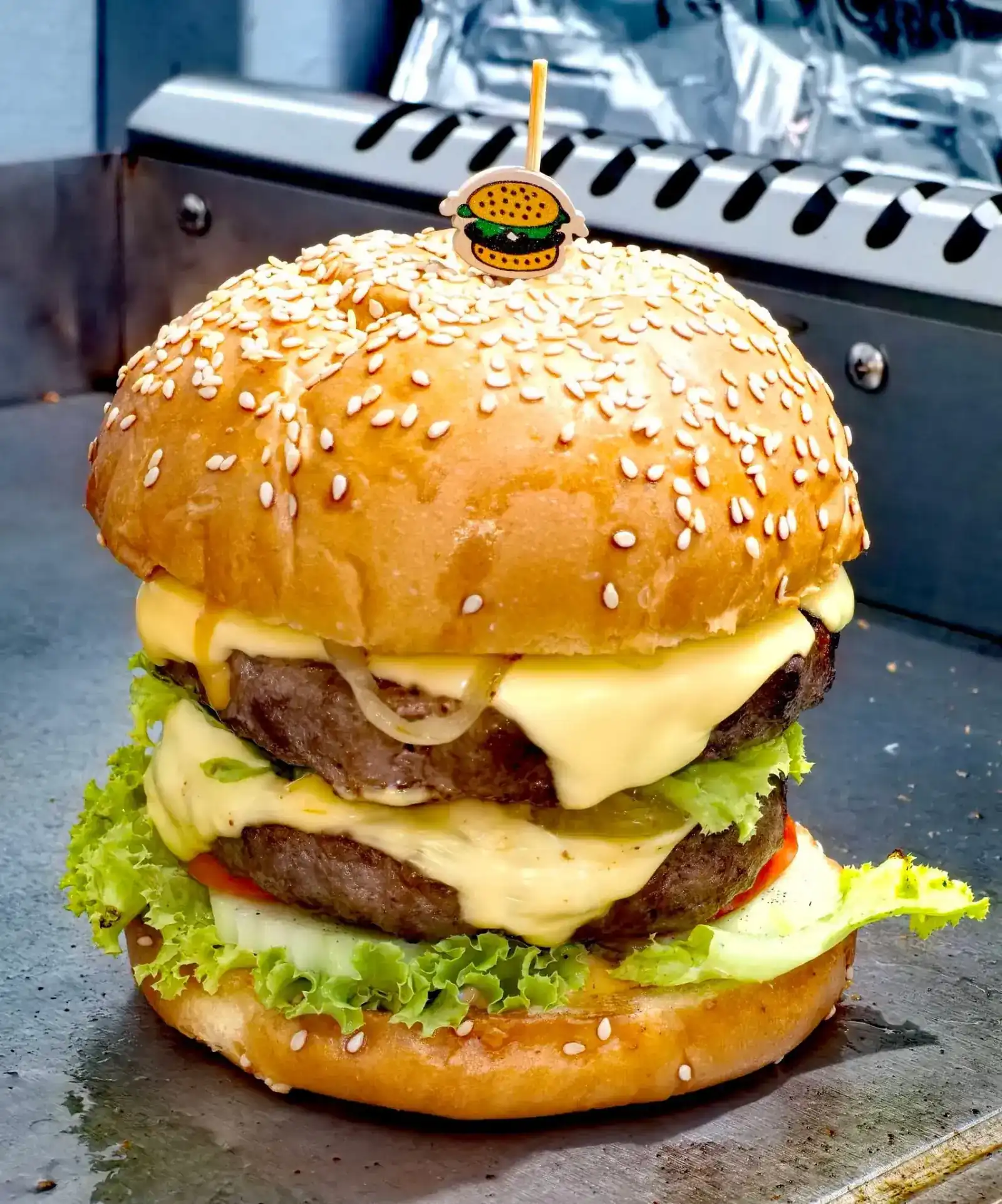A double cheeseburger with lettuce, tomato and onion on a sesame bun, on the grill at The WOLF