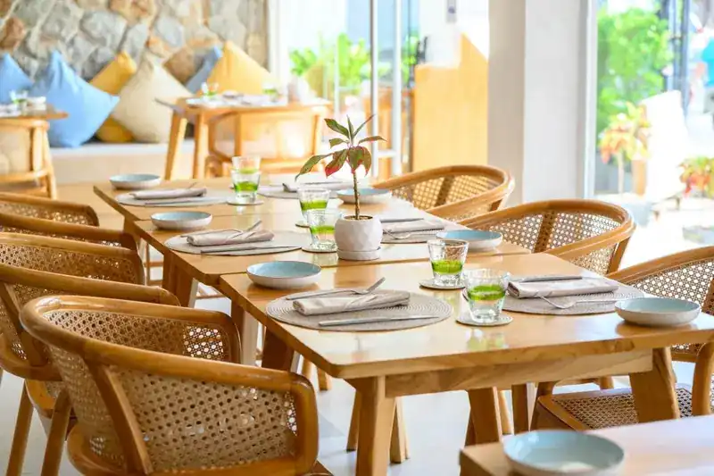 A long table set with blue plates and rattan armchairs inside the bright dining room
