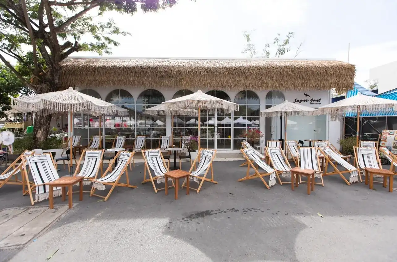 Sugar Goat from the street: a thatched roof over white arched windows, fringed parasols and striped deck chairs out front