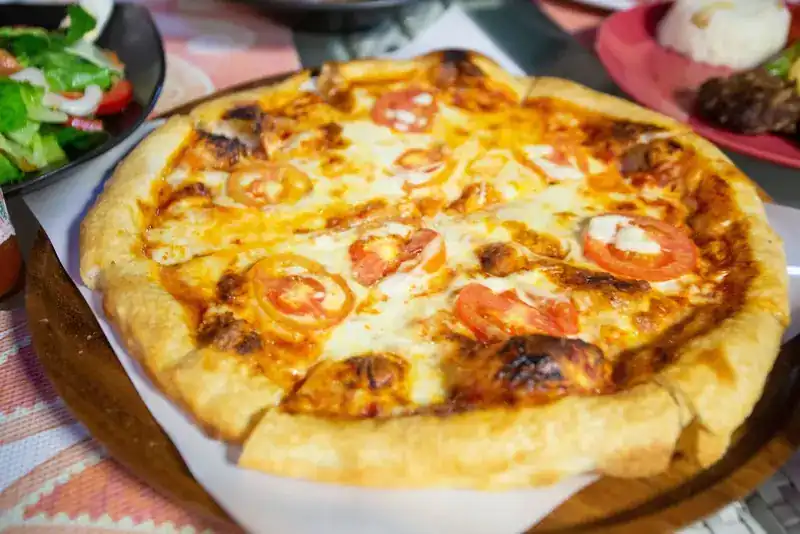 Pizza with tomato slices and melted cheese on a wooden board