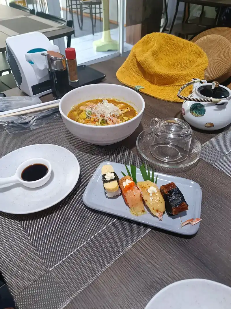 A plate of four nigiri, among them egg and salmon, with soy sauce and a bowl of soup