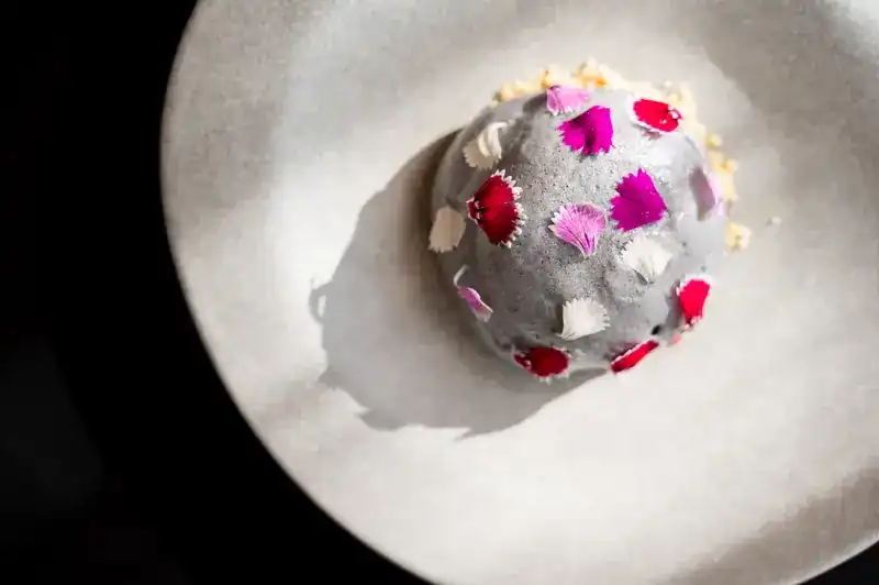 A grey dome scattered with pink and white petals on a pale plate