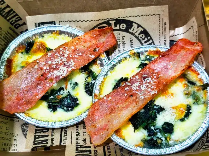 Two foil cups of baked spinach and cheese in a takeaway box