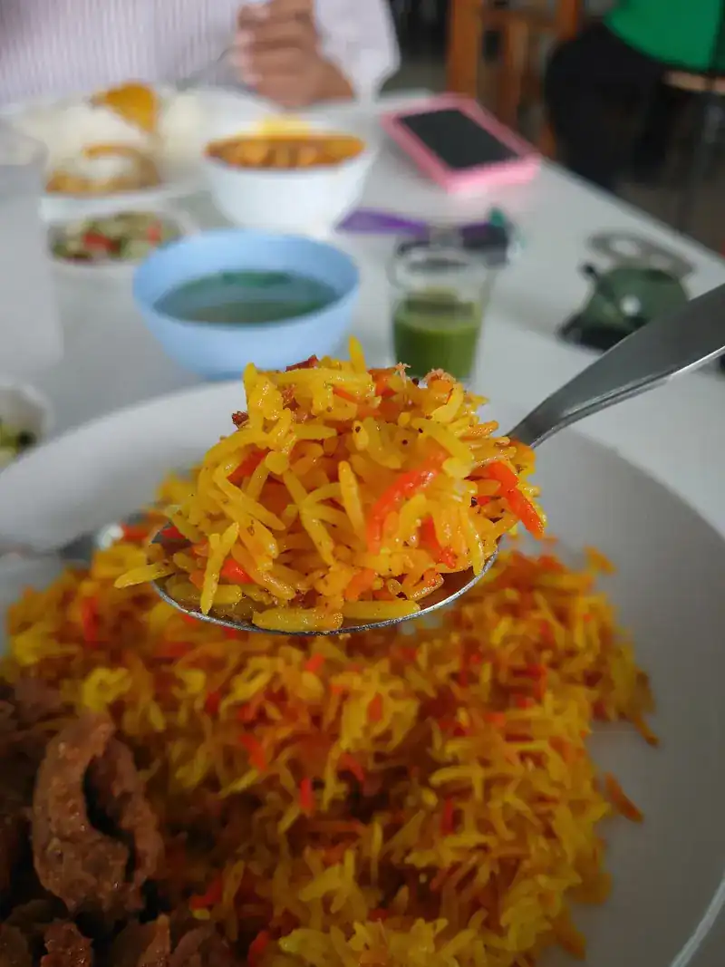 A spoonful of yellow biryani rice lifted from a plate with beef
