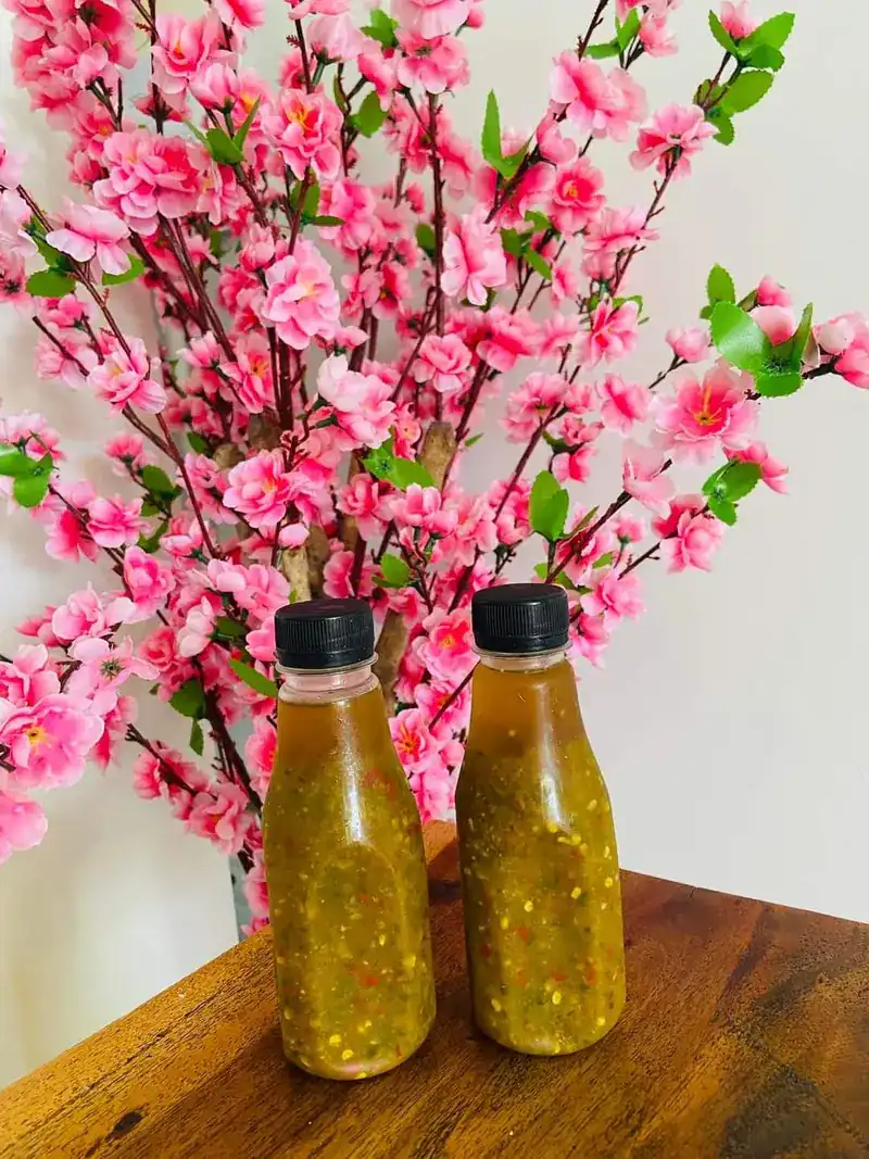 Two bottles of chilli sauce on a wooden table in front of pink blossom